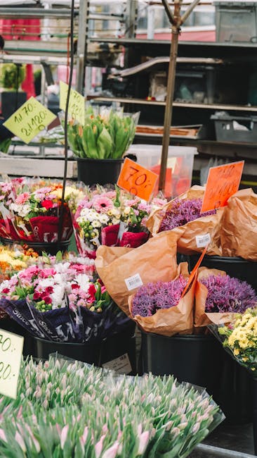 A vibrant display of fresh flower bouquets arranged on outdoor market stalls, featuring a variety of colorful blooms such as pink, white, and purple chrysanthemums, tulips, and lavender sprigs. The fl