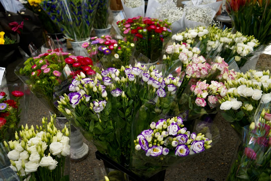 A diverse selection of fresh flowers arranged in bouquets and displayed on a countertop, featuring vibrant pink, purple, white, and red blooms including lisianthus, roses, and carnations. The flowers
